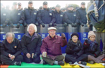 시민사회단체 대표들이 전경방패 앞 차가운 땅바닥에 앉아 구호를 외치고 있다. 